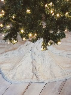 a white knitted blanket under a christmas tree with lights on it and a teddy bear in the middle