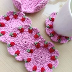 pink crocheted coasters with strawberries on them next to a white cup