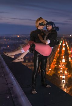 two people standing on top of a building at night, one holding the other's leg