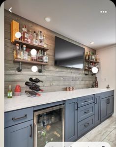 a kitchen with blue cabinets and shelves filled with liquor bottles on the wall, along with a flat screen tv