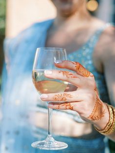 a woman holding a wine glass with hendix on her hands and arm, in front of a building