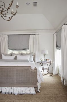 a bedroom with white bedding, curtains and a chandelier hanging from the ceiling