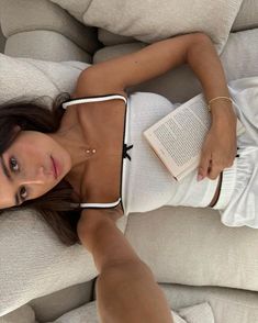 a woman laying on top of a white couch holding a book in her right hand