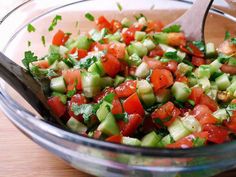 a glass bowl filled with cucumber and tomato salad on top of a wooden table