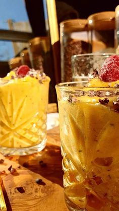 two glasses filled with dessert sitting on top of a wooden table next to each other