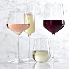 three different types of wine are lined up in glasses on a marble countertop, one is white and the other is red