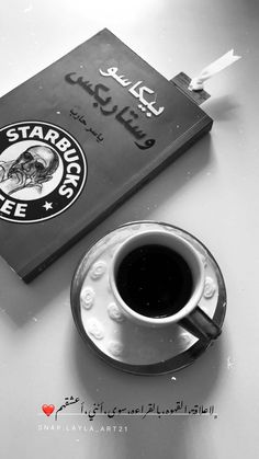 a black and white photo of a cup of coffee next to a book on a table