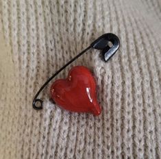 a red heart shaped brooch sitting on top of a white sweater