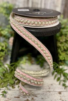 pink and white beaded ribbon on a black stand with greenery in the background