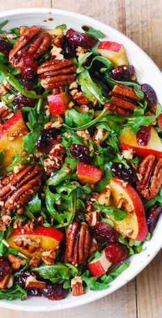 a salad with apples, pecans and cranberries in a white bowl on a wooden table