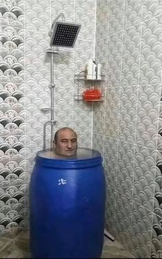 a man sitting in a large blue barrel next to a shower head and faucet