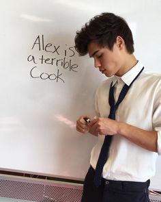 a young man writing on a whiteboard while wearing a tie and dress shirt with black pants