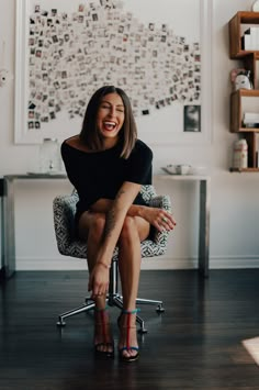 a woman sitting on top of a chair in front of a wall with pictures above her