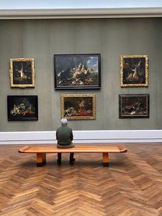 a person sitting on a bench in front of paintings