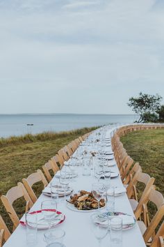 a long table is set up with plates and glasses for an outdoor dinner by the ocean