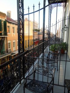 an outdoor balcony with wrought iron railings and chairs on the side walk, overlooking buildings