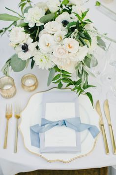 an elegant table setting with white flowers and blue napkins, gold cutlery and silverware