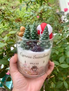 a hand holding a cup filled with small trees and candy canes on top of it