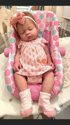 a baby girl sleeping in a pink and blue polka dot highchair with her eyes closed