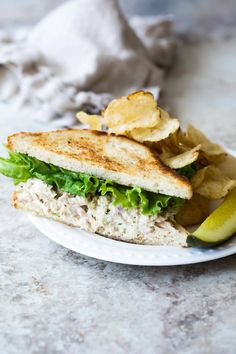 a white plate topped with a sandwich and chips next to a pickle on a table