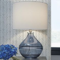 a blue vase sitting on top of a wooden table next to a lamp with a white shade