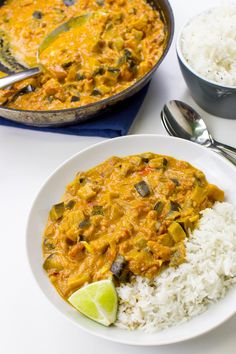 two plates with rice and curry on them next to a pot of white rice, spoons and silverware