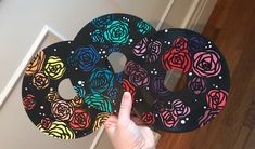 a hand holding two black paper plates with colorful roses on the front and sides, each decorated with different colors