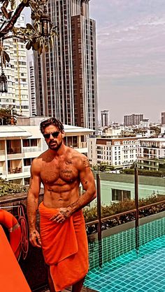 a man in an orange towel standing next to a swimming pool with buildings in the background