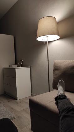 a person's feet resting on a couch under a lamp