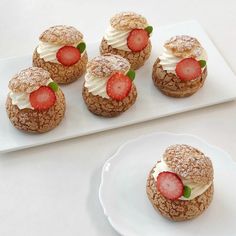 small pastries with strawberries on them sit on a white plate next to another one