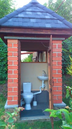 a toilet and sink in a small brick structure with an open door to the outside