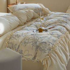 a bed with white linens and blue flowers on it, next to a glass of wine