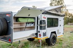 an off - road camper is parked in the grass with its door open and it's bed pulled out