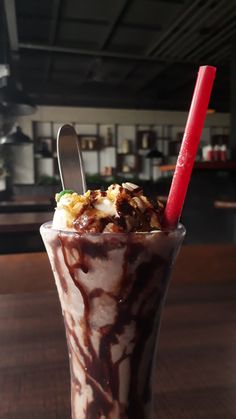 a chocolate milkshake with ice cream and toppings in a tall glass on a wooden table