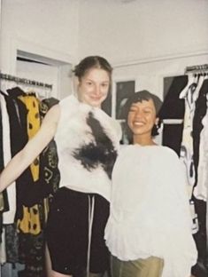 two women standing next to each other in front of clothes