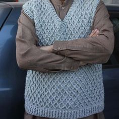 an old man standing in front of a car with his arms crossed and looking at the camera