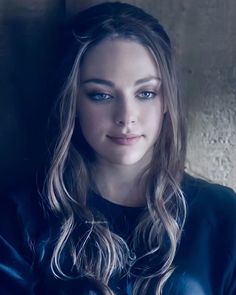 a woman with long hair and blue eyes is posing for a photo in front of a wall