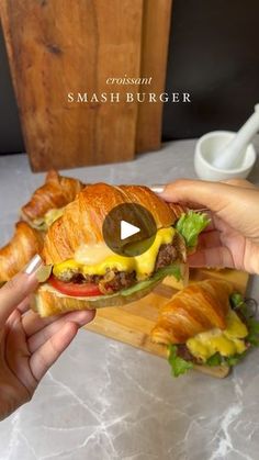 a person is holding a sandwich with cheese and lettuce on it while eating croissants