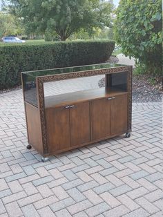 a wooden entertainment center sitting on top of a brick floor next to a tree and bushes