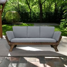 a couch sitting on top of a stone floor next to a wooden gazebo with trees in the background