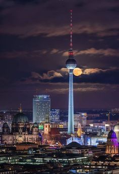 the berlin skyline is lit up at night, with an airplane in the sky above