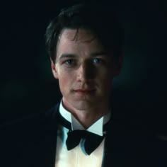 a man wearing a tuxedo and bow tie in the dark with his eyes wide open