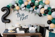 a table topped with balloons and cake next to a sign that says two fast on it