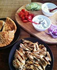 chicken and pita bread on plates with dips, tomatoes, cucumbers and onions