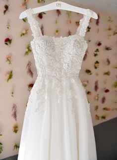 a white dress hanging on a hanger in front of a wall with pink flowers