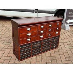 an old wooden dresser with many drawers on the top and bottom, in front of a white car