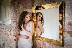 a woman standing in front of a brick wall looking at her reflection in a mirror