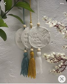 three tasseled ornaments hanging on a wall with flowers in the background and text below