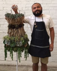 a man standing next to a plant display on a white brick wall holding an item in his hand