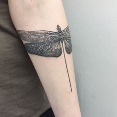 a black and white dragonfly tattoo on the right arm with an arrow in it